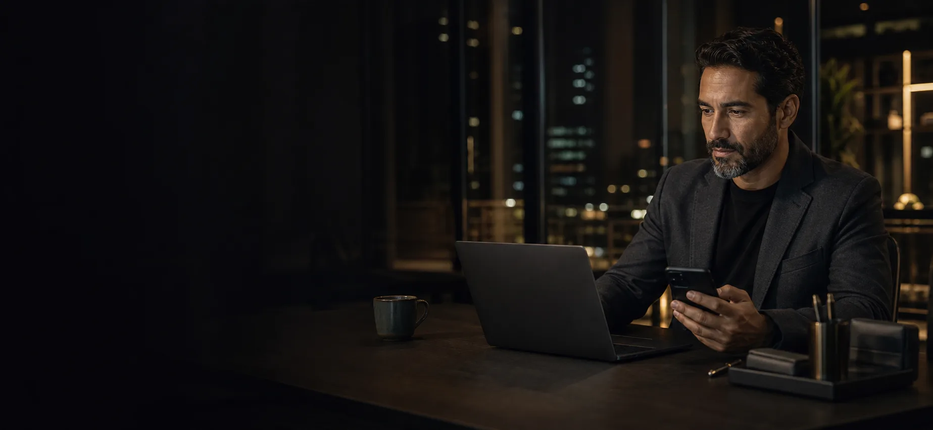 Empresário trabalhando à noite com notebook e celular em seu escritório